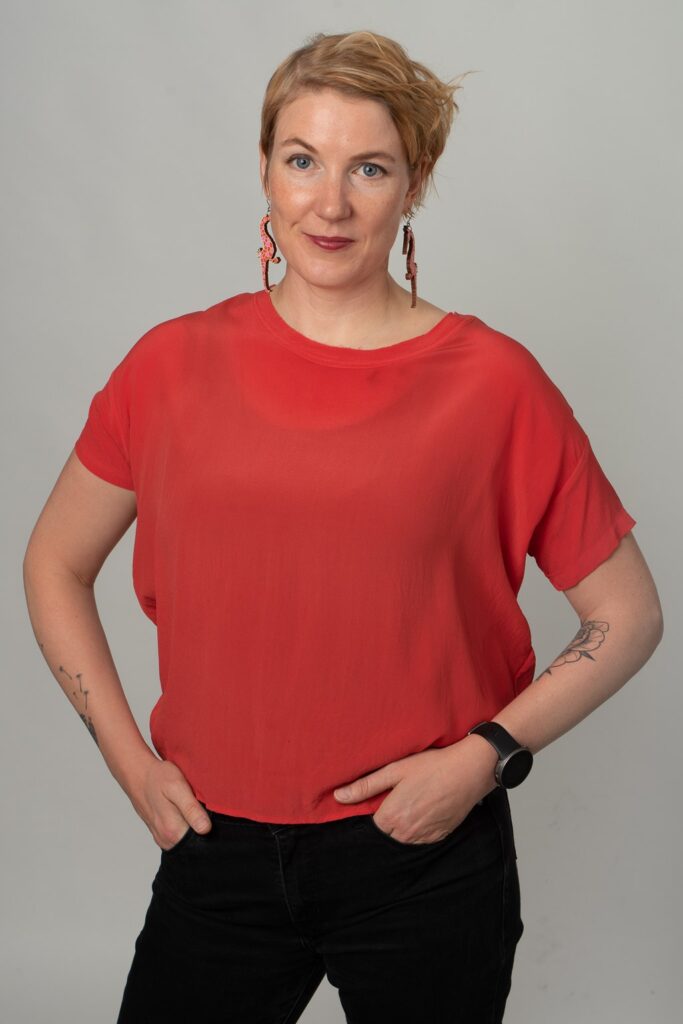 Hanna Ryti poseeraa oranssissa t-paidassa ja puisissa merihevos-korvakoruissa.